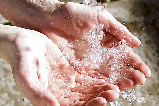 Hände, die unter eine Wasserquelle gehalten werden.