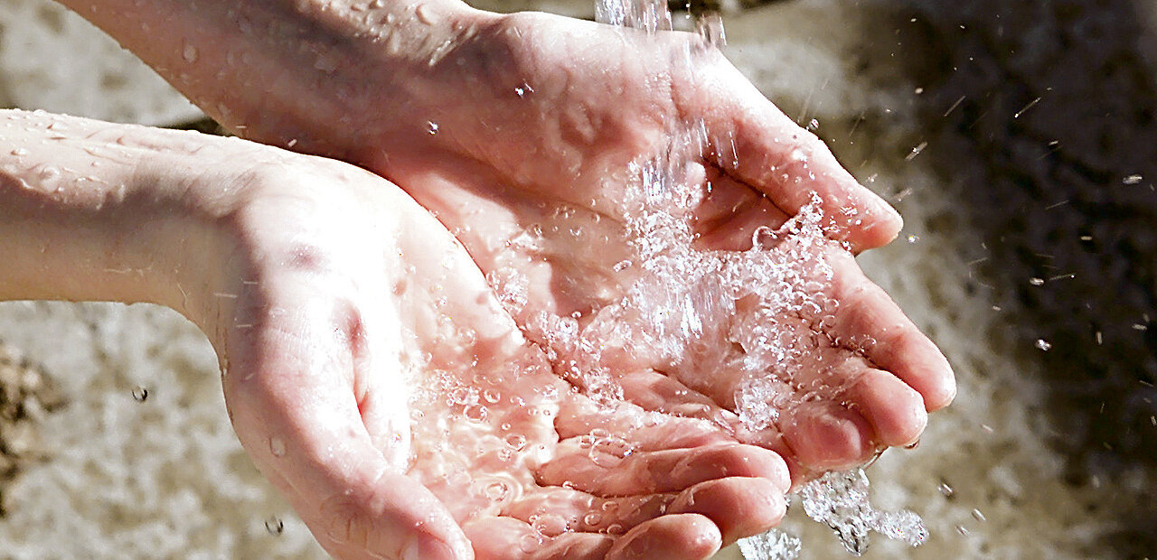 Hände, die unter eine Wasserquelle gehalten werden.