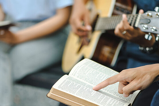 Jemand spielt Gitarre und zwei Personen lesen die Bibel