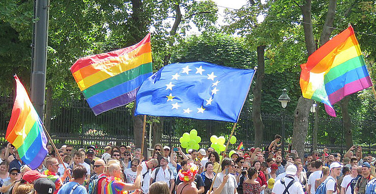 Regenbogenflaggen und eine EU-Flagge bei einer Demonstration.