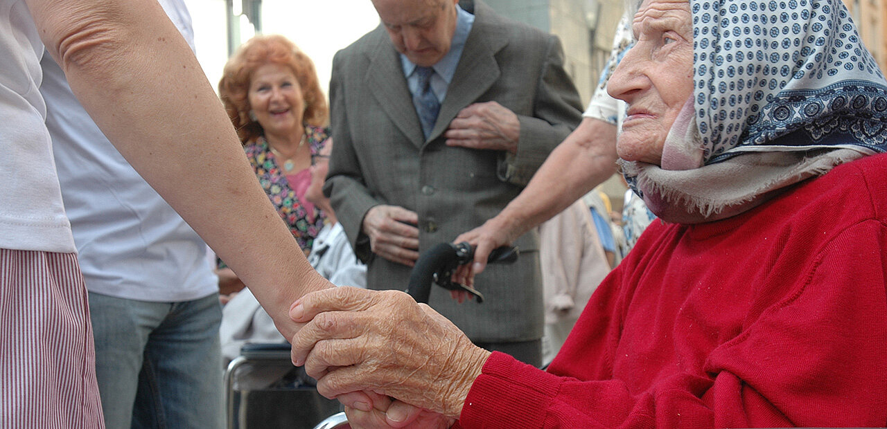 Alte Frau im Rollstuhl hält die Hand einer jüngeren Frau